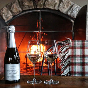 A bottle and two glasses of Westcott Vineyards Brilliant Sparkling Wine in front of the fireplace.