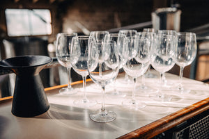 Twelve wine glasses and a pitcher on a white countertop.